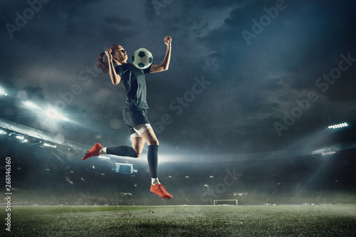 Młoda kobieta piłkarz lub piłkarz z długimi włosami w odzieży sportowej i buty kopanie piłki do bramki w skoku na stadionie. Pojęcie zdrowego stylu życia, profesjonalnego sportu, hobby, ruchu, ruchu