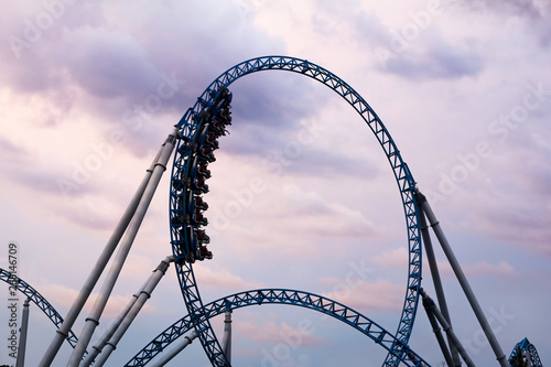 Silhouette of people having fun on a roller-coaster in an amusement park at sunset. Adrenalin concept. photo