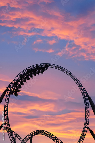 Silhouette of people having fun on a roller-coaster in an amusement park at sunset. Adrenalin concept. © belyaaa