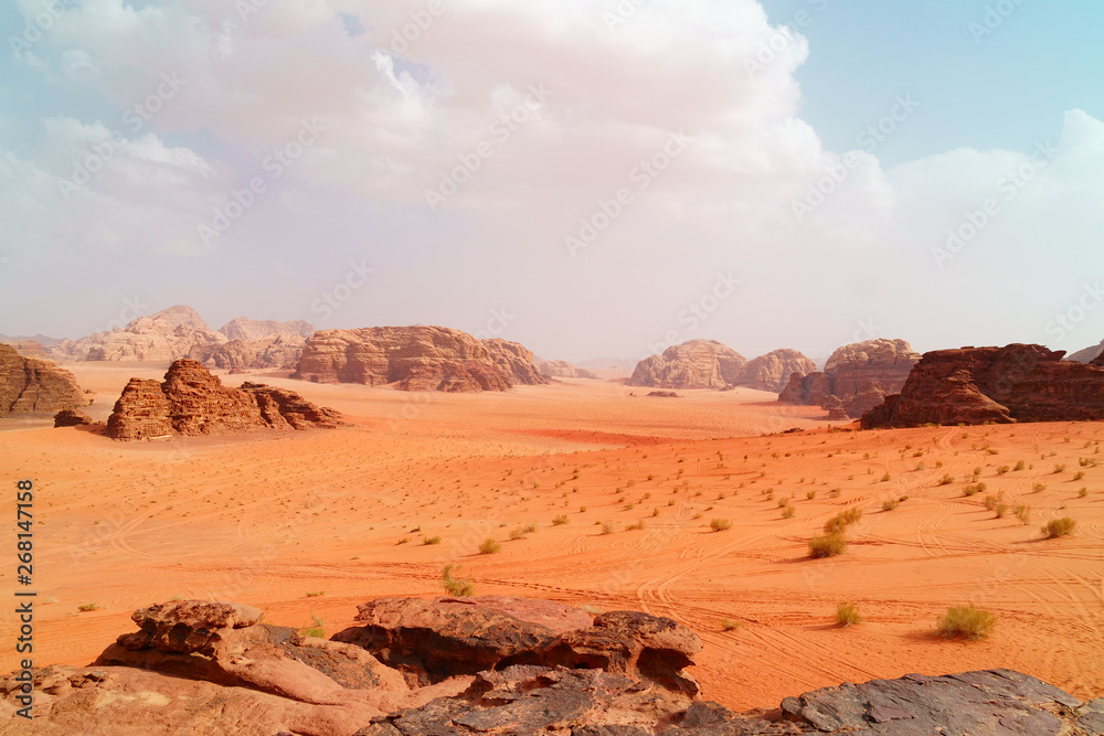 Wadi Rum desert, Jordan,  The Valley of the Moon. Orange sand, haze, clouds. Designation as a UNESCO World Heritage Site. National park outdoors landscape. Offroad adventures travel background.