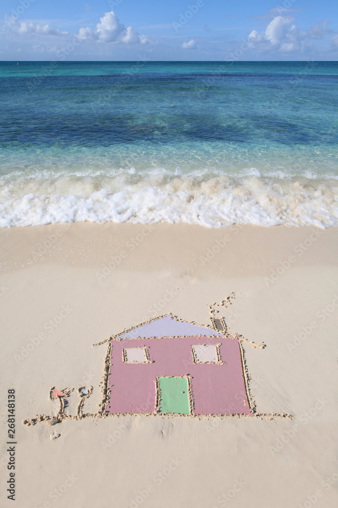 Fototapeta premium A house drawn in the sand on a beautiful sandy beach with waves lapping the shore. Symbol of moving house, moving overseas, new life.