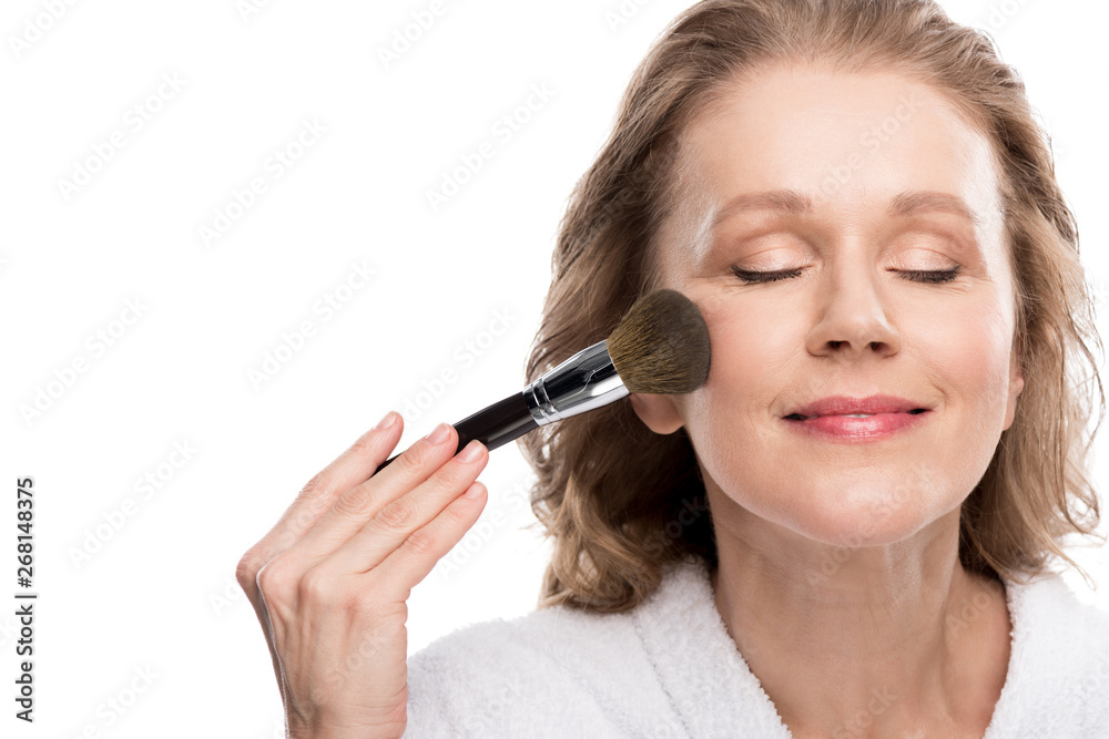 mature woman in bathrobe using cosmetics brush while applying makeup Isolated On White