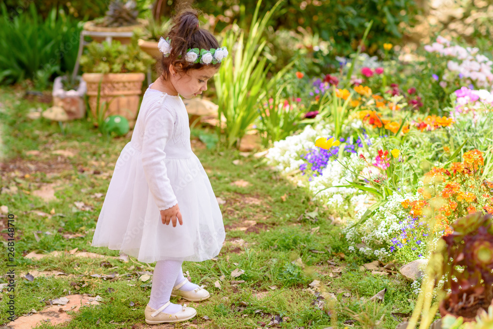 Side view full length portrait of beautiful little girl in white dress having fun a summer garden.