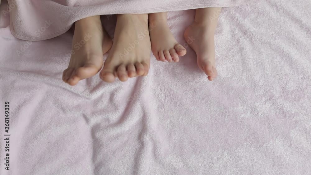 Two pairs of legs of the family in bed under the coverlet - mother and baby Two pairs of legs of the family in bed under the coverlet - mother and baby