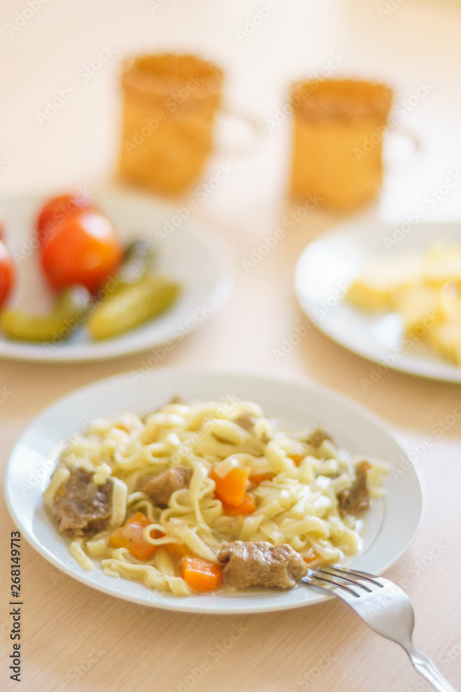 Macaroni with slices of meat and carrots. Marinated tomatoes and cucumbers. Cheese sliced in a plate. Two mugs on the table Macaroni with slices of meat and carrots. Marinated tomatoes and cucumbers. Cheese sliced in a plate. Two mugs on the table
