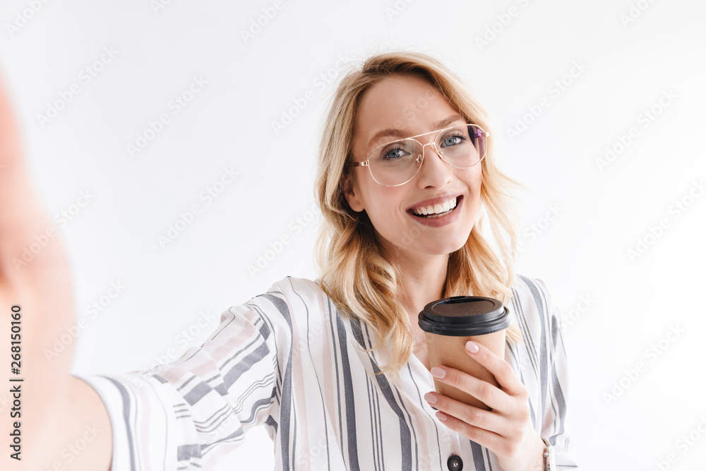 Photo of optimistic beautiful woman wearing glasses smiling at camera and holding paper cup Photo of optimistic beautiful woman wearing glasses smiling at camera and holding paper cup