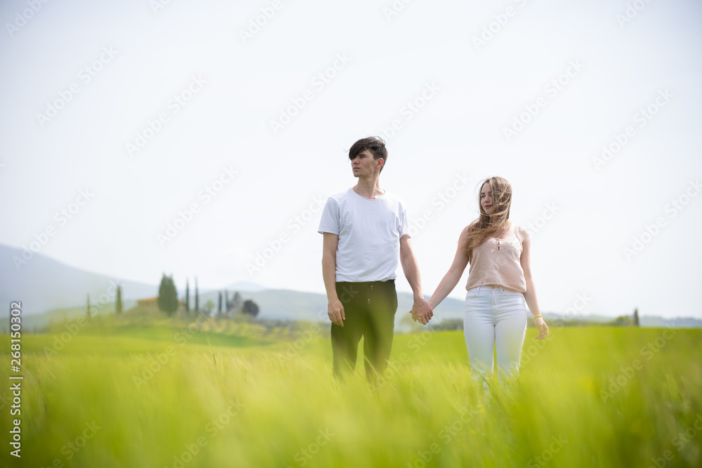 A young couple standing on a green field holding hands