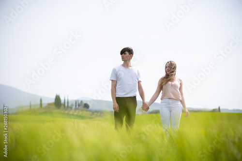 A young couple standing on a green field holding hands