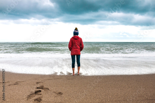 Barefoot woman looks at the winter sea.