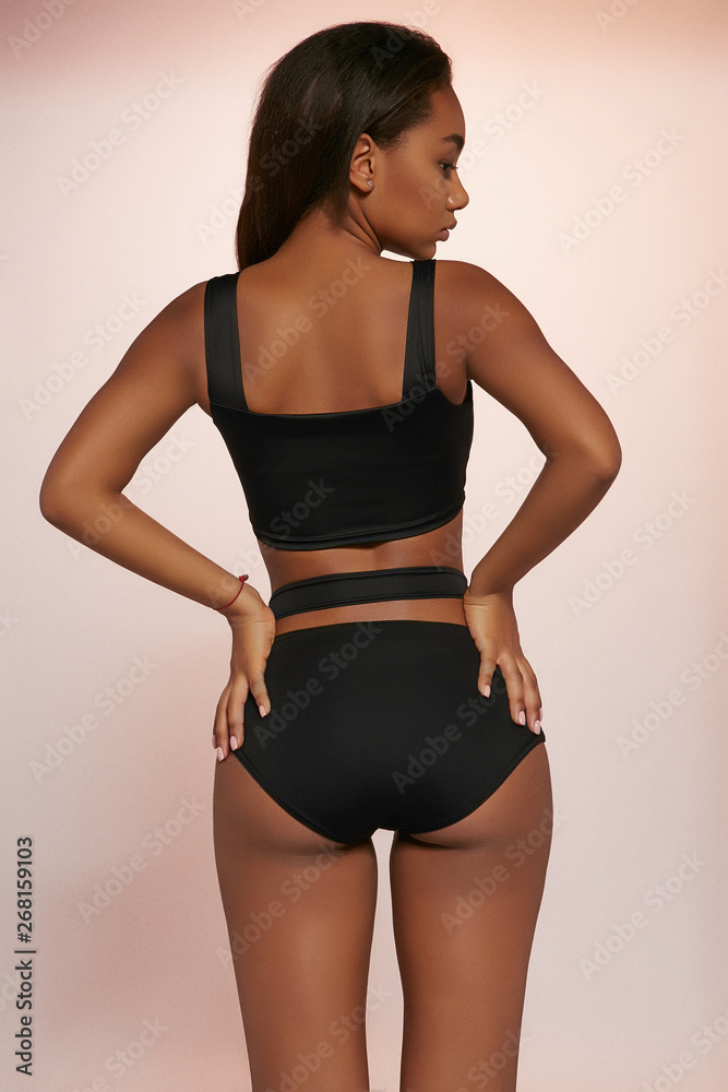 Three quarter back view shot of lady with dark hair, wearing black  two-piece swimsuit with