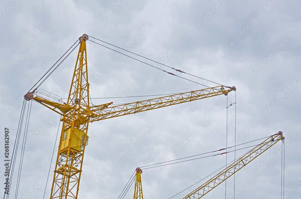 Two yellow construction crans on the cloudy sky background, the view from the bottom up. Two yellow construction crans on the cloudy sky background, the view from the bottom up.