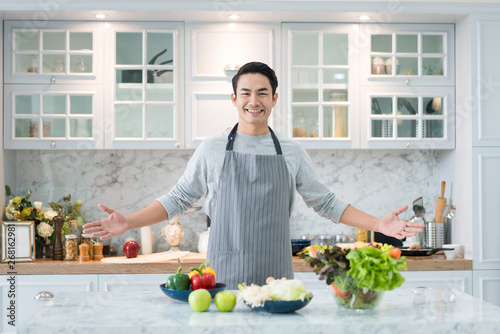 Asian handsome man cooking at home preparing salad in kitchen. Healthy eating, vegetarian food, diet and people concept