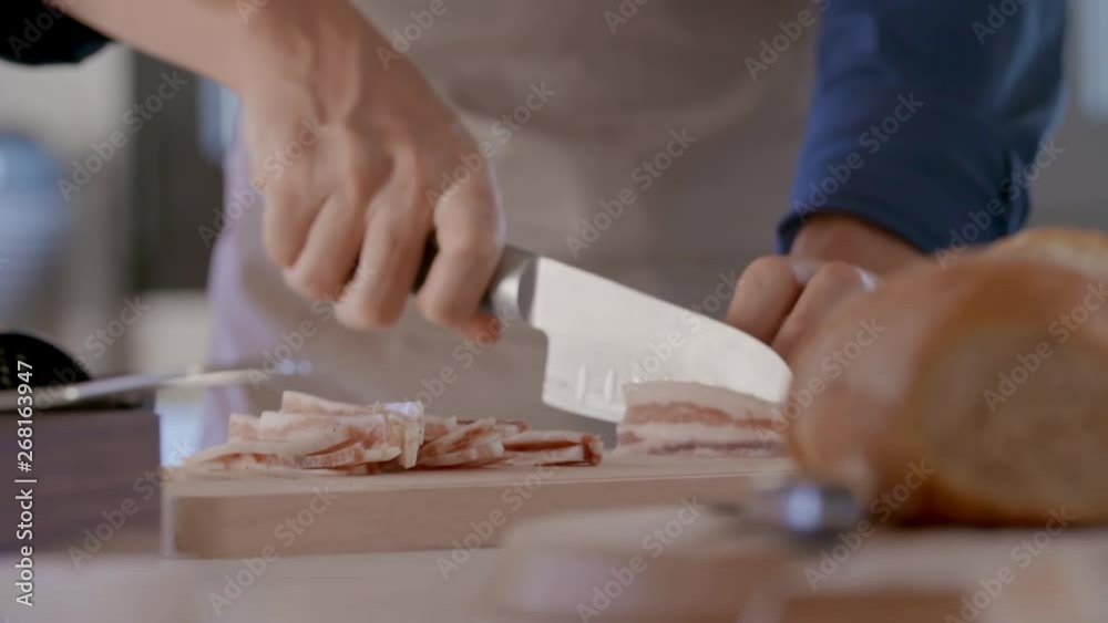 detail of man hand cutting jowl bacon with knife.Young people couple