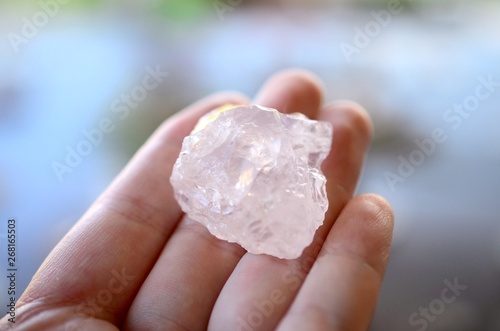 Woman's hand holding Rose Quartz, natural lighting. Pink, romantic healing crystal. Pastel rose quartz chunks. Person holding small pink gemstone. Light pink, rough and tumbled crystals. 