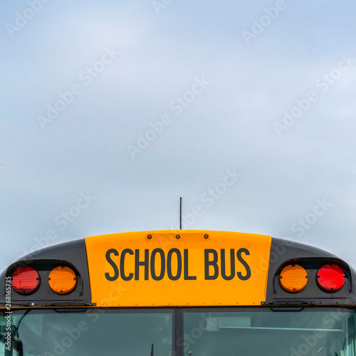 Square Front view of a yellow school bus with homes and cloudy sky in the background