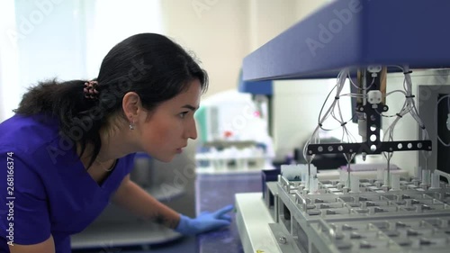 Portrait young lab woman in blue uniform and rubber gloves controlling drug manufacturing in the laboratory. Conducting research in the lab. Science, profession, healthcare. Slow motion photo