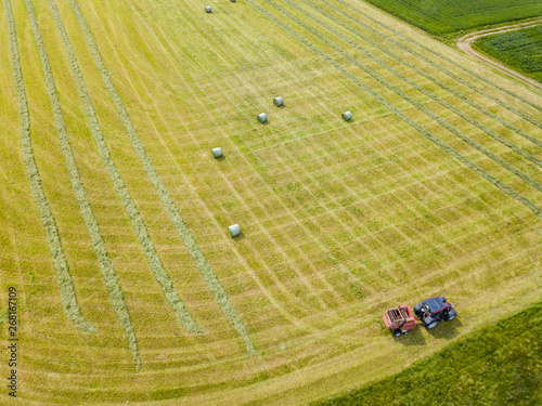 Aerial view of tractor harvesting green hay from meadow.