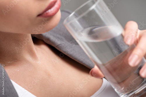 cropped view of young woman holding glass of water while suffering from heat on grey