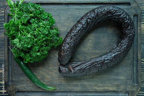 Blood sausage on a dark cutting board decorated with curly parsley. Blood sausage. View from above. Dark wooden background.