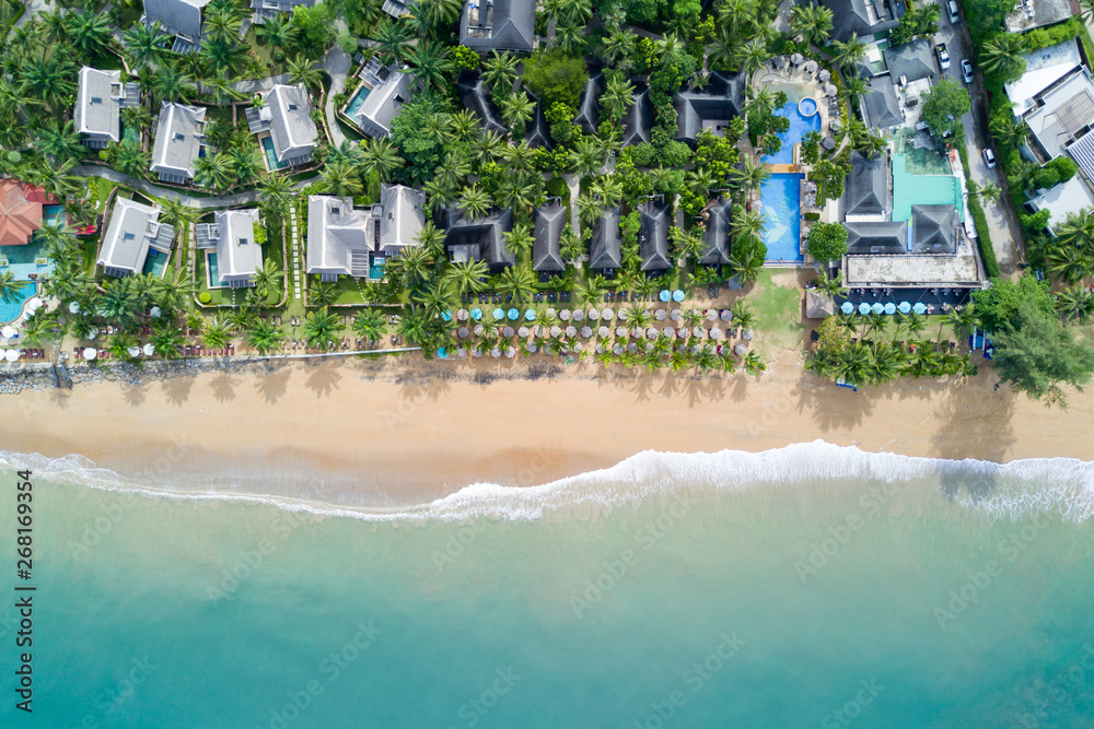 Aerial view of resort villa planning with coconut trees, umbrellas and deck chairs on the beach. Beautiful ocean wave reaching coastline from top view. Andaman sea in Thailand. Summer holiday concept