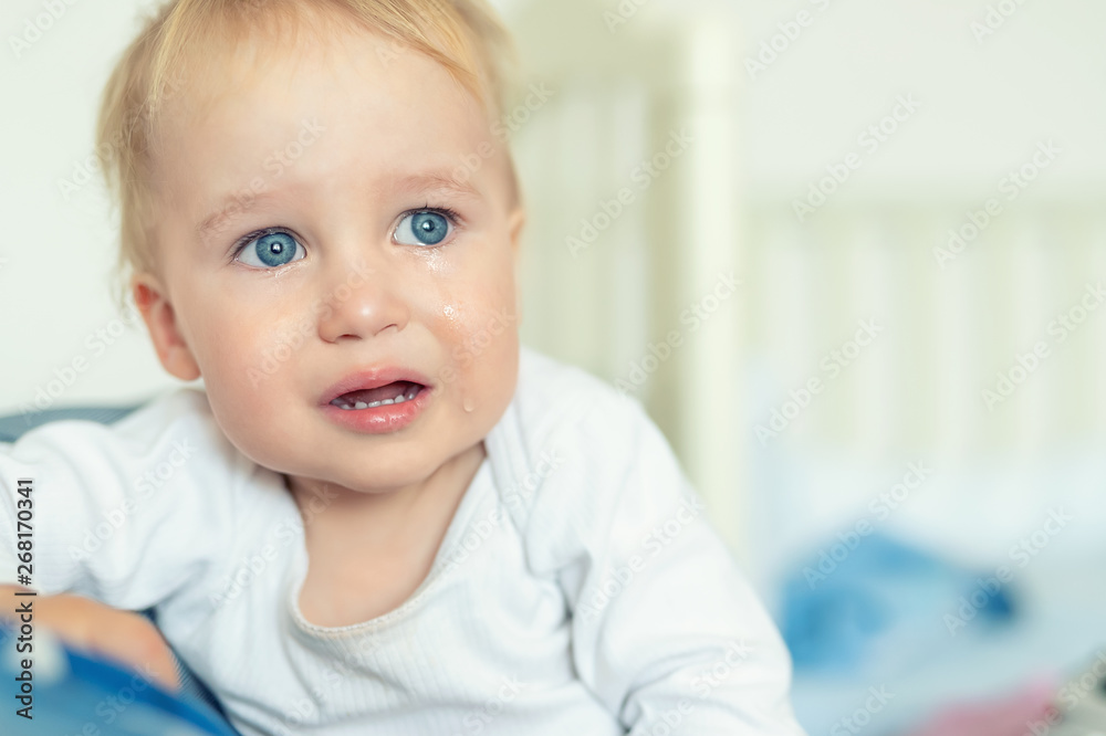 Cute caucasian blond toddler boy portrait crying at home during hysterics. Little child feeling sad. Small pensive baby after quarell