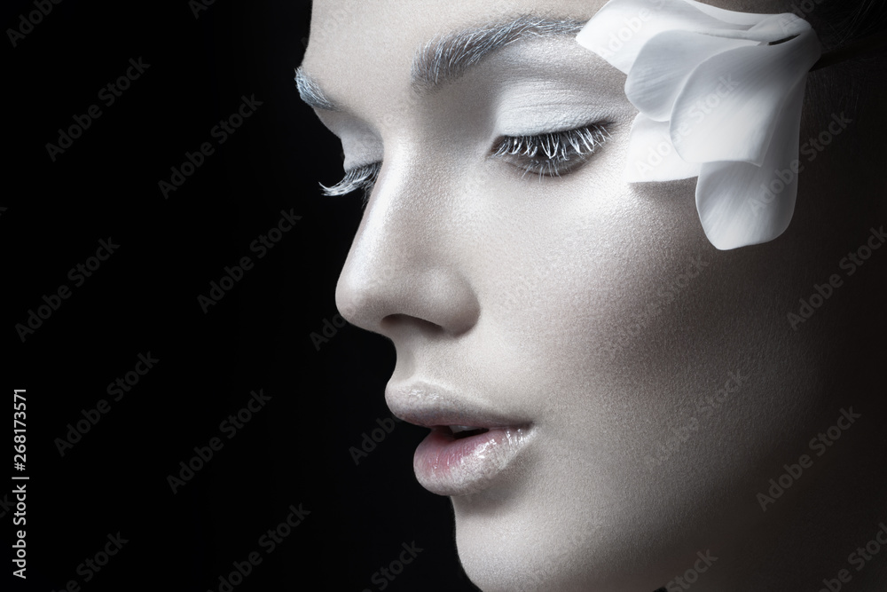 Beauty portrait. Tender girl with fragile white makeup, anf flowers near ear, looking down, Concept salon makeup, cosmetics, isolated on black background. - obrazy, fototapety, plakaty 
