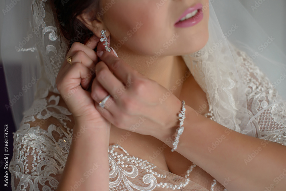 Beautiful bride in white lace wedding dress and embroidered veil wearing vintage diamond jewelry and adjusting earring clasp, getting ready for the wedding day or bridal accessories promoting concept