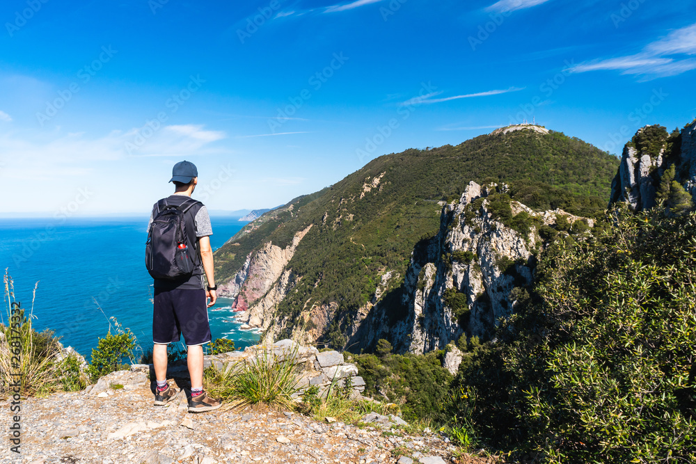 Male hiker amazed by the stunning view from the Muzzerone Mountain peak over the Ligurian Sea rugged coastline, in Porto Venere, La Spezia, Italy. Hiking on a lovely summer day.