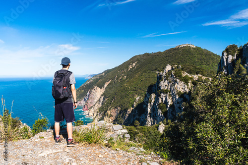 Male hiker amazed by the stunning view from the Muzzerone Mountain peak over the Ligurian Sea rugged coastline, in Porto Venere, La Spezia, Italy. Hiking on a lovely summer day.
