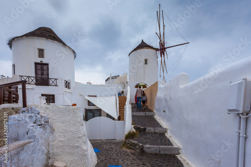 Tourists near windmill in the colorful village of Oia on a rainy day