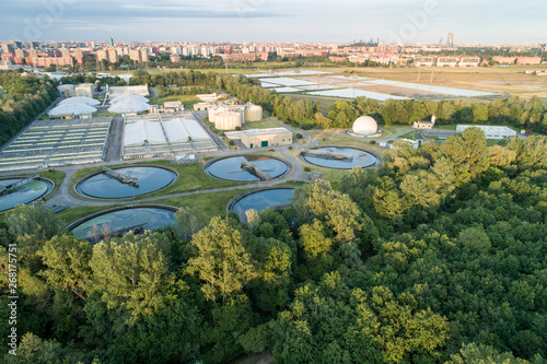 Flying over sewage treatment plant. Aerial view of industrial water treatment for the city in background. Waste water purification.