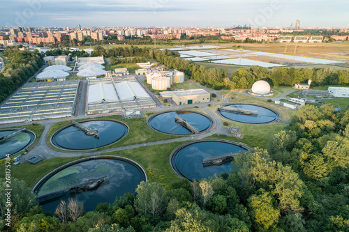Flying over sewage treatment plant. Aerial view of industrial water treatment for the city in background. Waste water purification.
