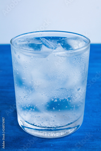  Transparent glass with water and ice cubes on a blue background