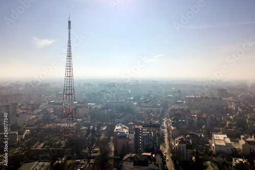 Aerial view of modern city urban foggy landscape with tall television tower on bright blue sky copy space background at dawn. Drone photography.