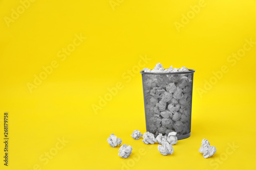 Metal bin with crumpled paper on color background, space for text