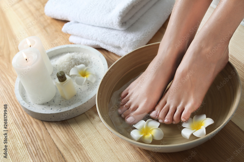 Closeup view of woman soaking her feet in dish with water and flowers on wooden floor. Spa treatment Closeup view of woman soaking her feet in dish with water and flowers on wooden floor. Spa treatment
