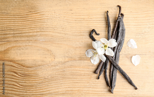 Flat lay composition with aromatic vanilla sticks and flowers on wooden background. Space for text