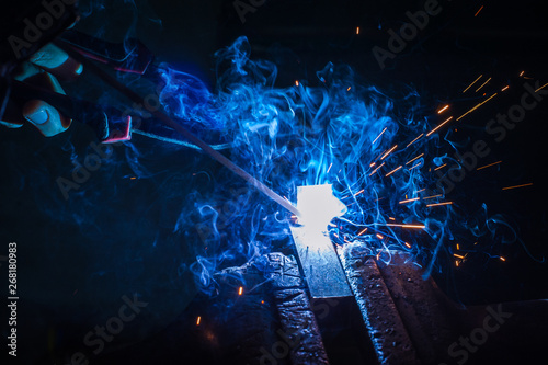 Worker with protective gloves welding metal part in workshop