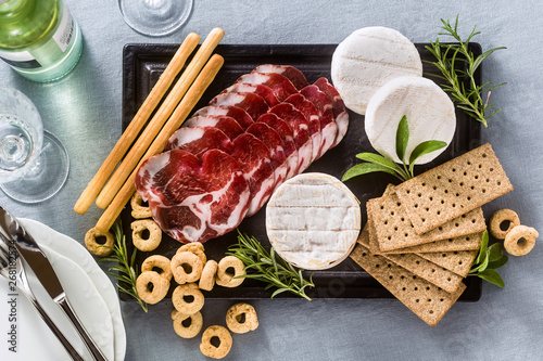 cold cuts and cheese are served on a tray on a table with white wine, crackers, grissini and taralli with aromatic herbs on a blue linen festive tablecloth. photo