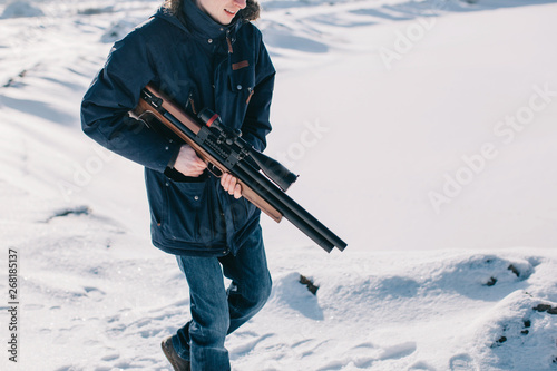 Unrecognizable man walking by the snow with rifle