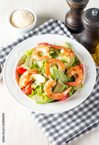 Fresh shrimp salad made of tomato, ruccola, avocado, prawns, chicken breast, arugula, crackers and spices. Caesar salad in a white, transparent bowl on wooden background