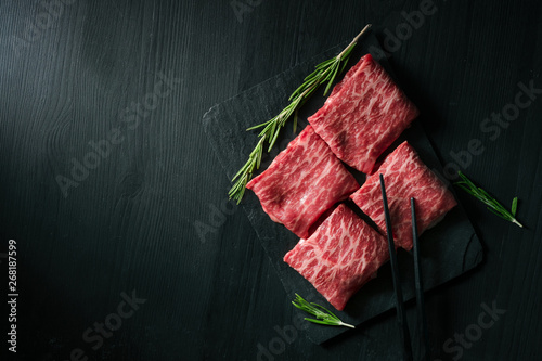 Sliced wagyu marbled beef for yakiniku on plate on black background, Premium Japanese meat, top view and copy space photo