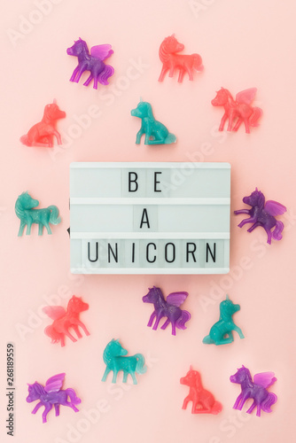 Light box saying Be a Unicorn surrounded by colorful toy unicorns on a pink background