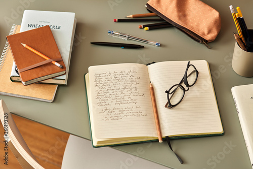 Notebook with handwritten text, pencil and glasses on desk. photo