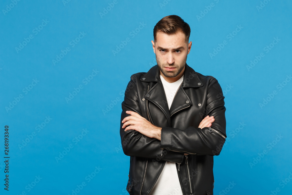 Young sad frustrated worried unshaven man in black jacket white t-shirt looking camera isolated on blue wall background studio portrait. People sincere emotions lifestyle concept. Mock up copy space. Young sad frustrated worried unshaven man in black jacket white t-shirt looking camera isolated on blue wall background studio portrait. People sincere emotions lifestyle concept. Mock up copy space.