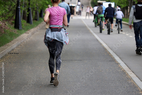 Slim sexy girl running on a road in a summer park. Sporty lifestyle, concept of jogging, workout, active people