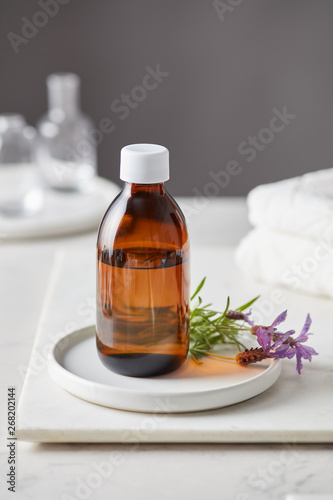 Brown glass bottle with lavender flower on plate.