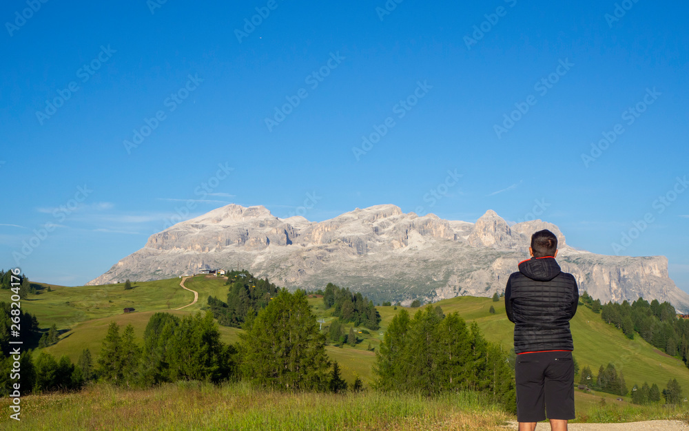 A person admires the fantastic Dolomites in Italy during the summer period. The massive Sella in the background. Hiker photographed from behind. Dolomites a Unesco World Heritage