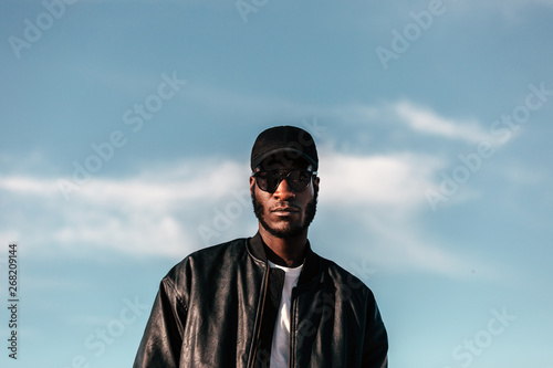 Young black man wearing black cap and sunglasses looking at came photo