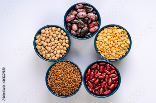 A variety of legumes. Lentils, chickpeas, peas and beans in blue bowls on a white background. Top view.